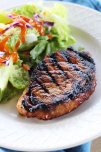 A grilled marinated pork chop on a plate with a salad