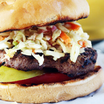 A juicy grilled hamburger with tomatoes, pickles and topped with sweet + tangy cabbage slaw.