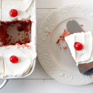 Cherry cake in a baking pan next to a plate with a piece of cake.