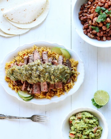 A white wooden table with a platter of steak, rice, beans, salsa, and more