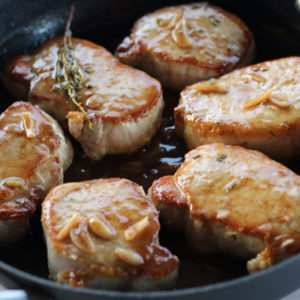 Pork Chops being fried in a skillet with sauce