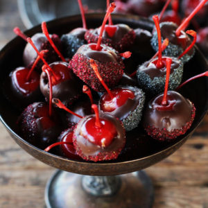 A close up shot of rum spiked maraschino cherries dipped in dark chocolate and dusted with sparkling sugar