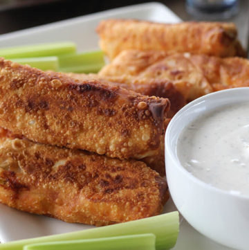 Buffalo Chicken Egg Rolls on a white serving platter served with ranch dressing and fresh celery.